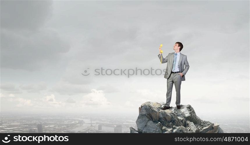 Man with phone receiver. Smiling businessman talking on yellow phone handset on rock top