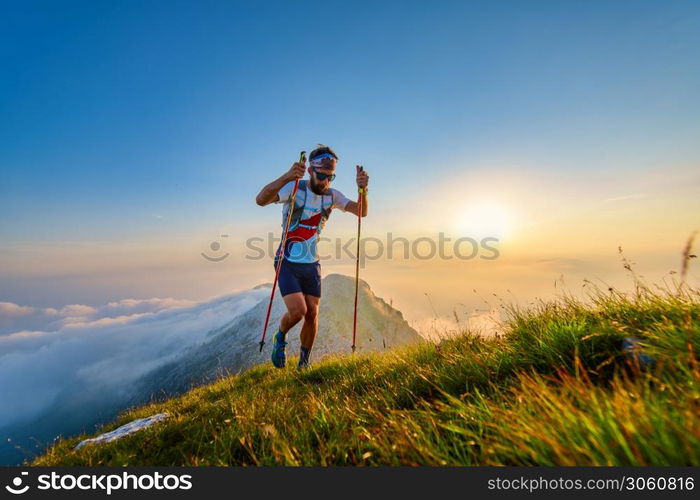 Man with poles in the mountains with sunset behind