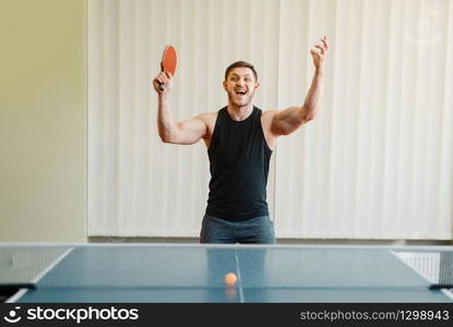 Man with racket in hand wins ping pong tournament indoors. Male person in sportswear, training in table tennis club