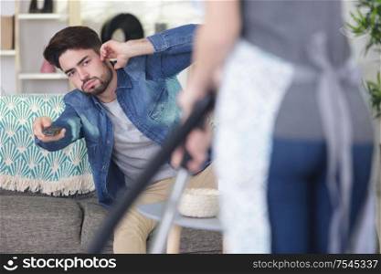 man with remote-control trying to watch-tv behind wife hoovering