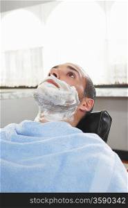 Man with shaving foam on face at barbers