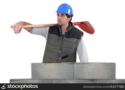 Man with spade stood by unfinished wall