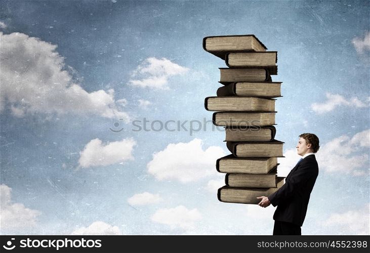 Man with stack of books in hands. Young businessman carrying stack of old books in his hands