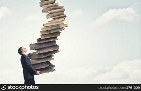 Man with stack of books in hands. Young businessman carrying stack of old books in his hands