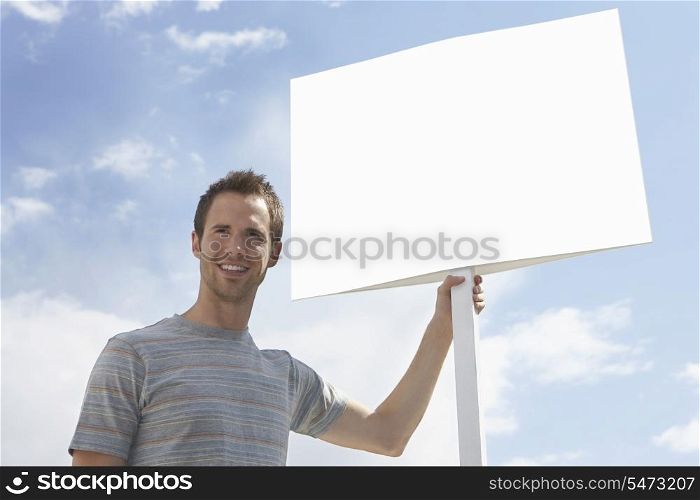 Man with standing by blank sign against cloudy sky