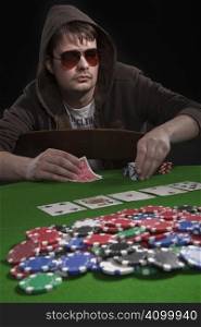 Man with sun glasses playing poker on green table. Chips and cards on the table.