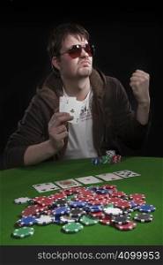 Man with sun glasses playing poker on green table. Chips and cards on the table.