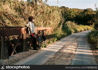 Man with surgical mask in the field with his bicycle during de-escalated in spain by covid-19 on a metal bridge