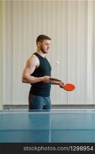 Man with two rackets stuffs blows in ping pong indoors. Male person in sportswear at the table with net, training in table-tennis club
