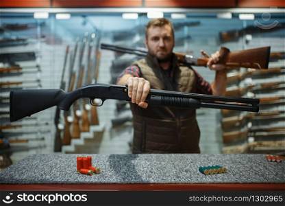 Man with two rifles at counter in gun shop. Euqipment for hunters on stand in weapon store, hunting and sport shooting hobby. Man with two rifles at counter in gun shop