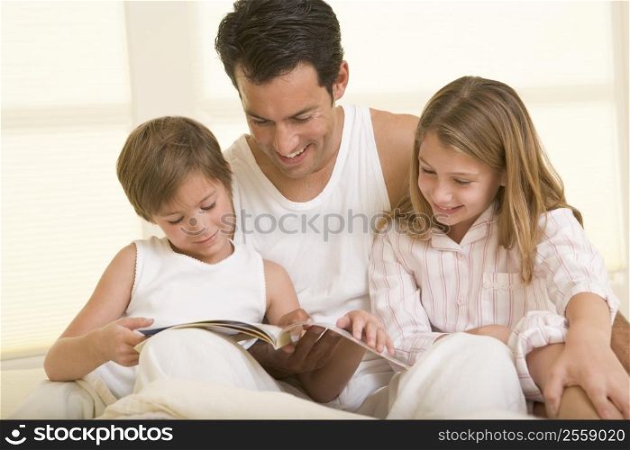Man with two young children sitting in bed reading a book and smiling