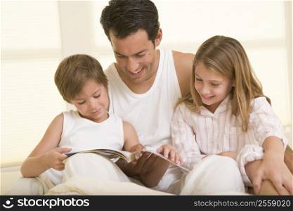 Man with two young children sitting in bed reading a book and smiling