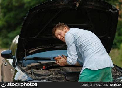 Man with wheel brace standing at the opened hood, car breakdown. Broken automobile or repairing of vehicle, trouble with auto on highway. Man with wheel brace standing at the opened hood