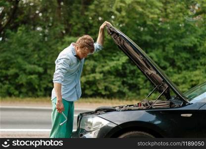 Man with wheel brace standing at the opened hood, car breakdown. Broken automobile or repairing of vehicle, trouble with auto on highway