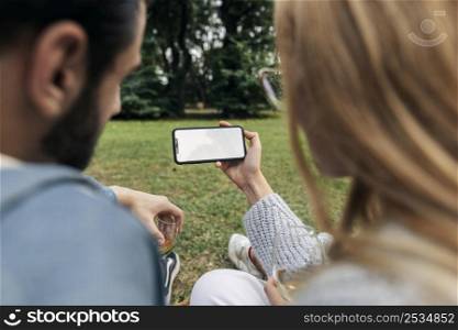 man woman looking phone while having picnic outdoors
