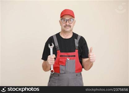 man worker in a black t shirt, glasses and red gray construction overall holds a new gray tool straight pipe wrench or spanner and giving a thumbs up on a white isolated background.. man worker in a black t shirt, glasses and red gray construction overall holds a new gray tool straight pipe wrench or spanner and giving a thumbs up on a white isolated background
