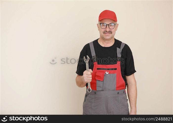 man worker in a black t shirt, glasses and red gray construction overall holds a new gray tool straight pipe wrench or spanner on a white isolated background.. man worker in a black t shirt, glasses and red gray construction overall holds a new gray tool straight pipe wrench or spanner on a white isolated background