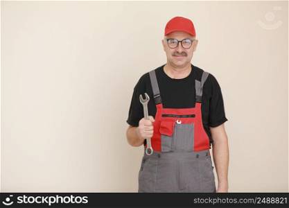 man worker in a black t shirt, glasses and red gray construction overall holds a new gray tool straight pipe wrench or spanner on a white isolated background.. man worker in a black t shirt, glasses and red gray construction overall holds a new gray tool straight pipe wrench or spanner on a white isolated background