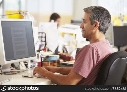 Man Working At Desk In Busy Creative Office