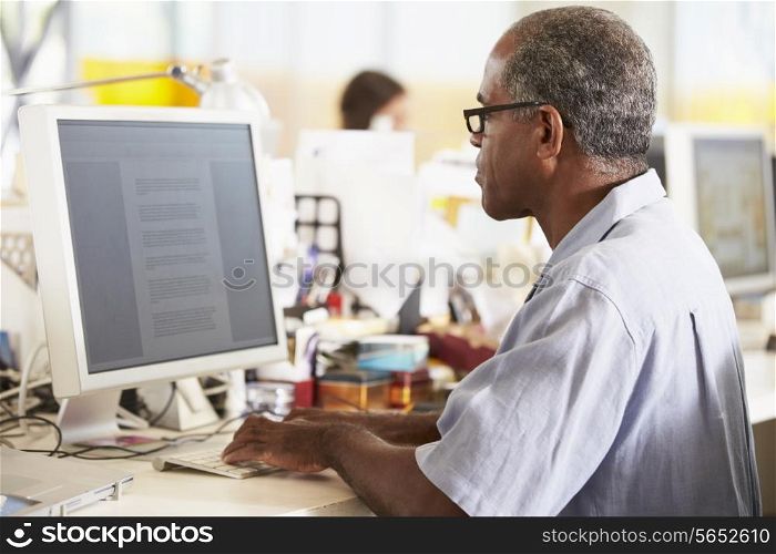 Man Working At Desk In Busy Creative Office