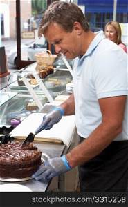 Man Working Behind Counter In Cafe Slicing Cake