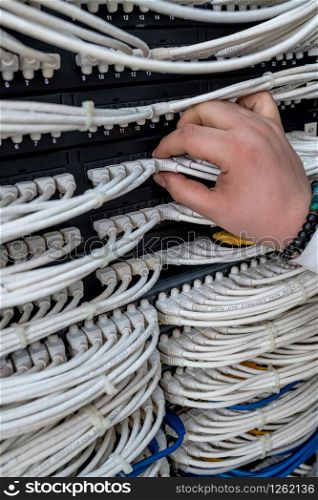 man working in network server room with fiber optic hub for digital communications and internet. network switch hand