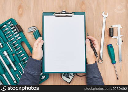 Man working in workshop holding clipboard using many tools. Wrench, spanner, calliper and ratchet with many attachments. Work tools. Universal tool set. Professional equipment