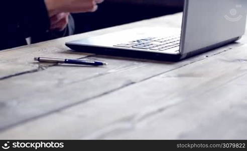 Man working on a laptop on a rustic wooden table, hands close up