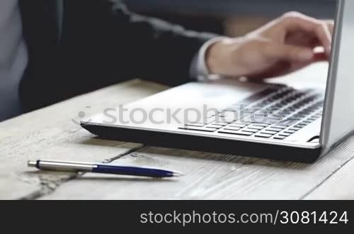 Man working on a laptop on a rustic wooden table, hands close up