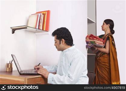 Man working on laptop and woman keeping clothes in cupboard