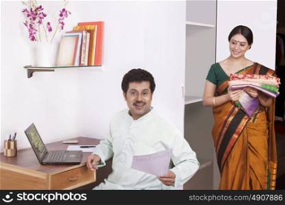 Man working on laptop and woman keeping clothes in cupboard
