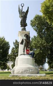 Man working on laptop sitting on the Confederate Soldiers of Arkansas monument. In front of the state capital.