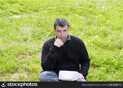 man working on meadow grass with notebook computer black winter sweater