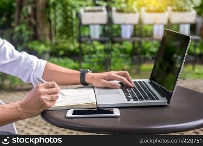 Man working on modern laptop sitting outside natural hardwood desk with green flora background sunlight day outdoor, everywhere you are from laptop concept