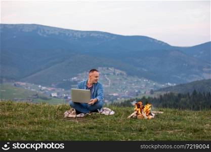 Man working outdoors with laptop sitting in mountains. Concept of remote work or freelancer lifestyle. Cellular network broadband coverage. internet 5G. Hiker tourist enjoying valley view.. Man working outdoors with laptop sitting in mountains. Concept of remote work or freelancer lifestyle. Cellular network broadband coverage. internet 5G. Hiker tourist enjoying valley view
