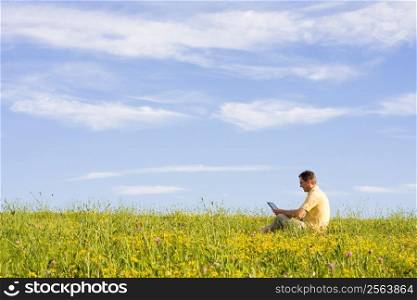 Man working with laptop in a meadow of flowers