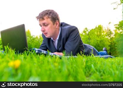 man working with laptop lying on the lawn