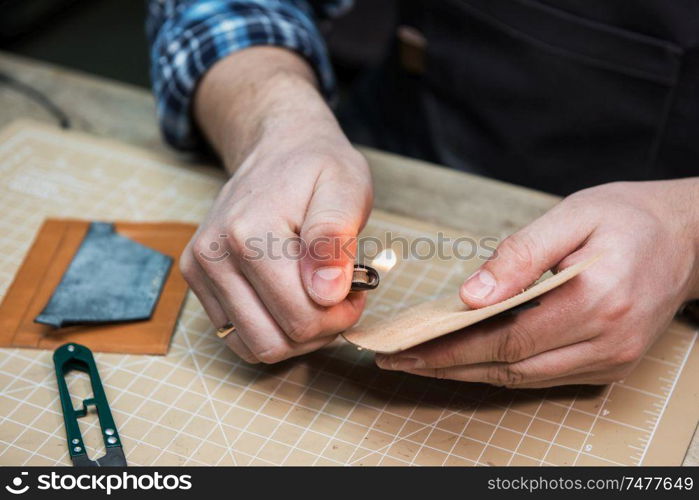 Man working with leather textile at a workshop. Worker burns the edges of the thread after sewing. Concept of handmade craft production of leather goods.. Concept of handmade craft production of leather goods.
