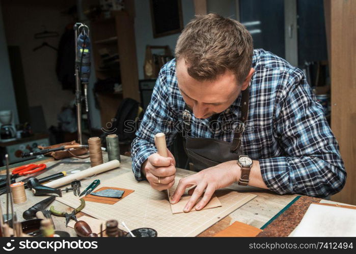 Man working with leather textile at a workshop. Craftman cutting leather. Concept of handmade craft production of leather goods.. Concept of handmade craft production of leather goods.