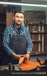 Man working with leather textile at a workshop. Male portrait. Concept of handmade craft production of leather goods.. Concept of handmade craft production of leather goods.