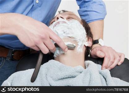 Man wrapped in towel being shaved by barber over colored background
