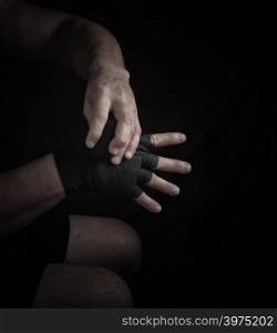 man wraps his hands in black textile bandage for sports, black background