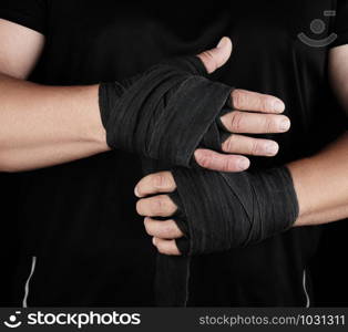 man wraps his hands in black textile bandage for sports, black background, copy space