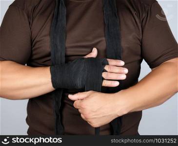 man wraps his hands in black textile bandage for sports, white background, close up