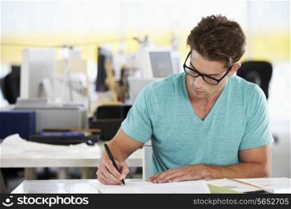 Man Writing At Desk In Busy Creative Office