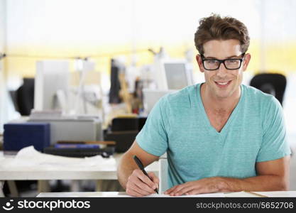Man Writing At Desk In Busy Creative Office