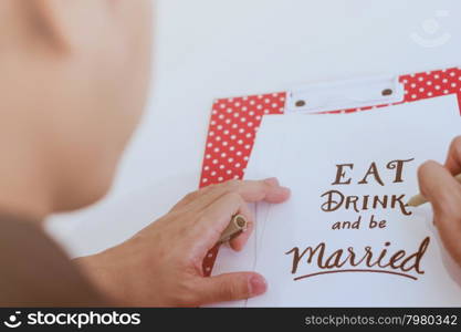 Man writing eat drink and be married quote on paper card for wedding concept