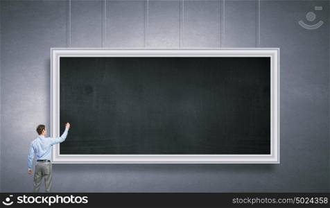 Man writing on chalkboard. Businessman standing with back and drawing on blank chalkboard