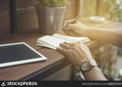 man writing on notebook with digital tablet on wooden table, selective focus and vintage tone