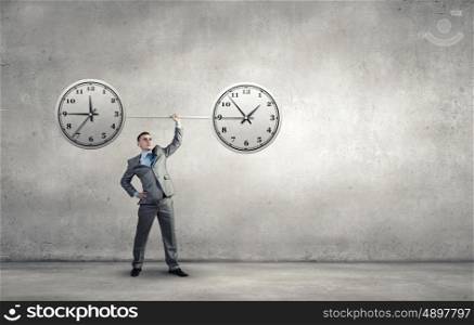 Manage your time. Confident businessman lifting above head barbell with clock